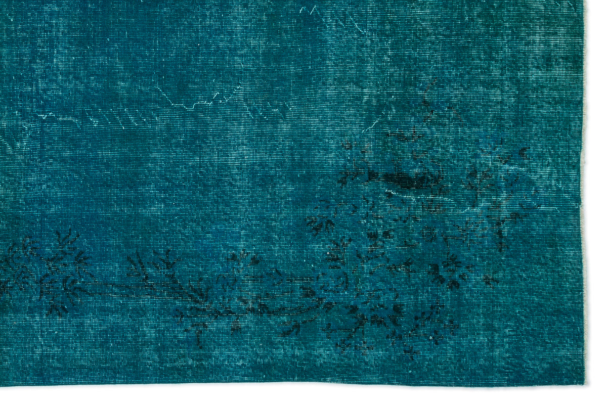 Teal distressed rug with a faded black floral pattern and visible horizontal weave texture.