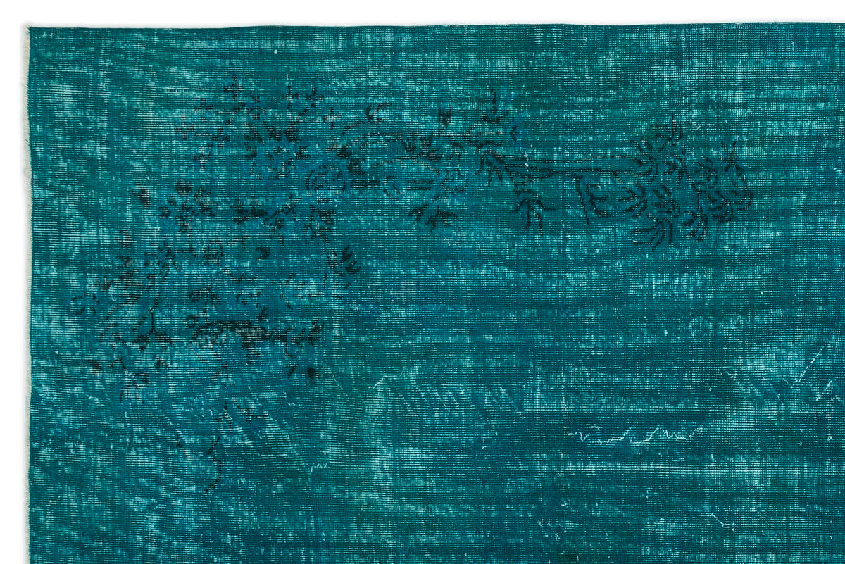 Teal rug with a distressed, faded floral pattern in black, featuring a visible woven texture.