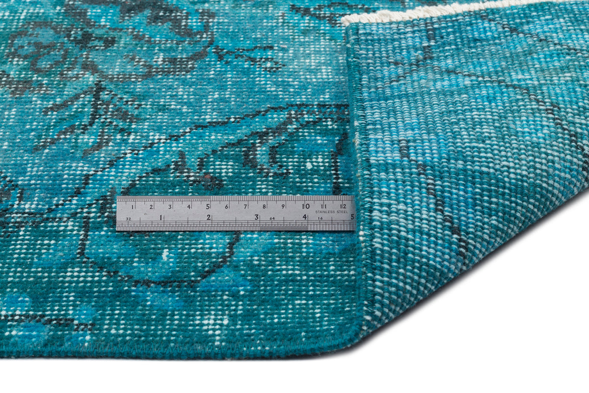 Teal and black distressed floral rug with a folded corner and a stainless steel ruler for scale.