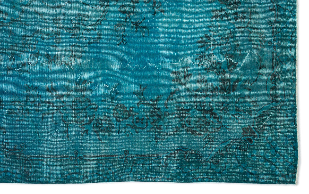 Teal distressed rug with a faded black floral pattern and a decorative border.