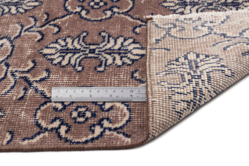 Load image 1 in gallery view. Brown and navy blue floral patterned rug with a folded corner revealing the woven backing and a metal ruler for scale.