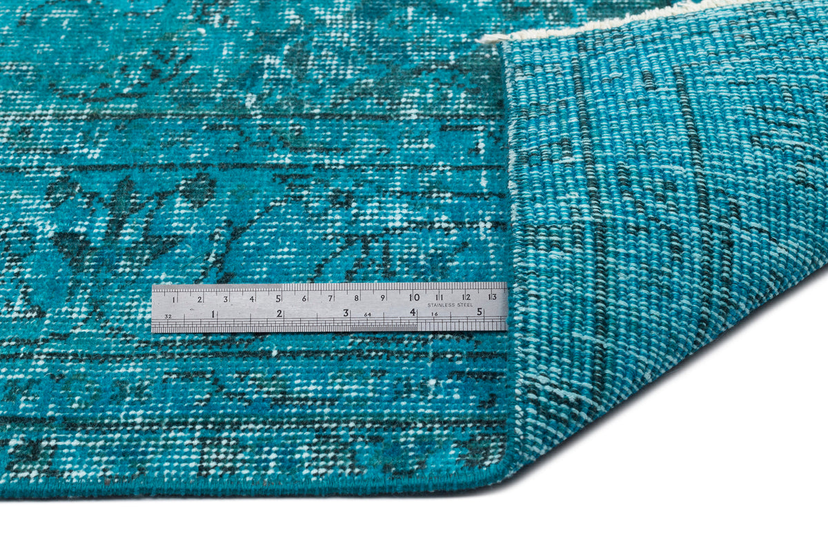 Teal and black distressed medallion rug with a folded corner and a stainless steel ruler for scale.