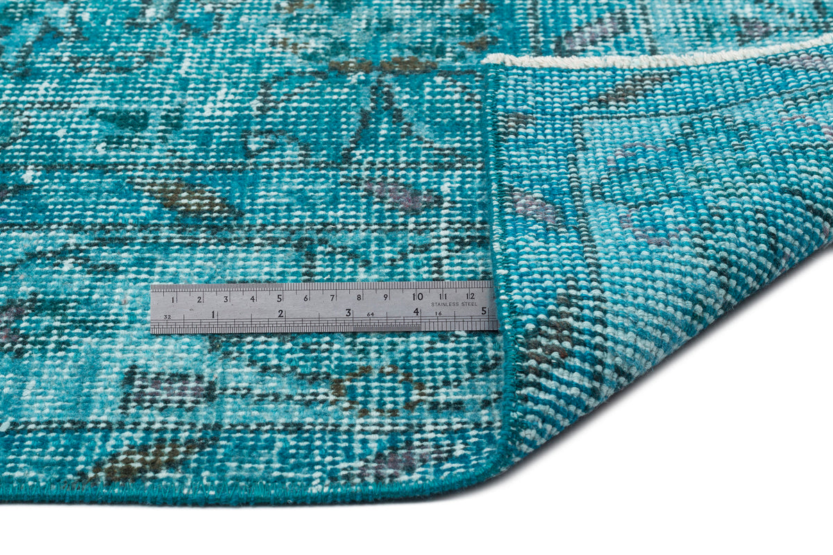 Teal and white distressed medallion rug with a folded corner and a metal ruler for scale.