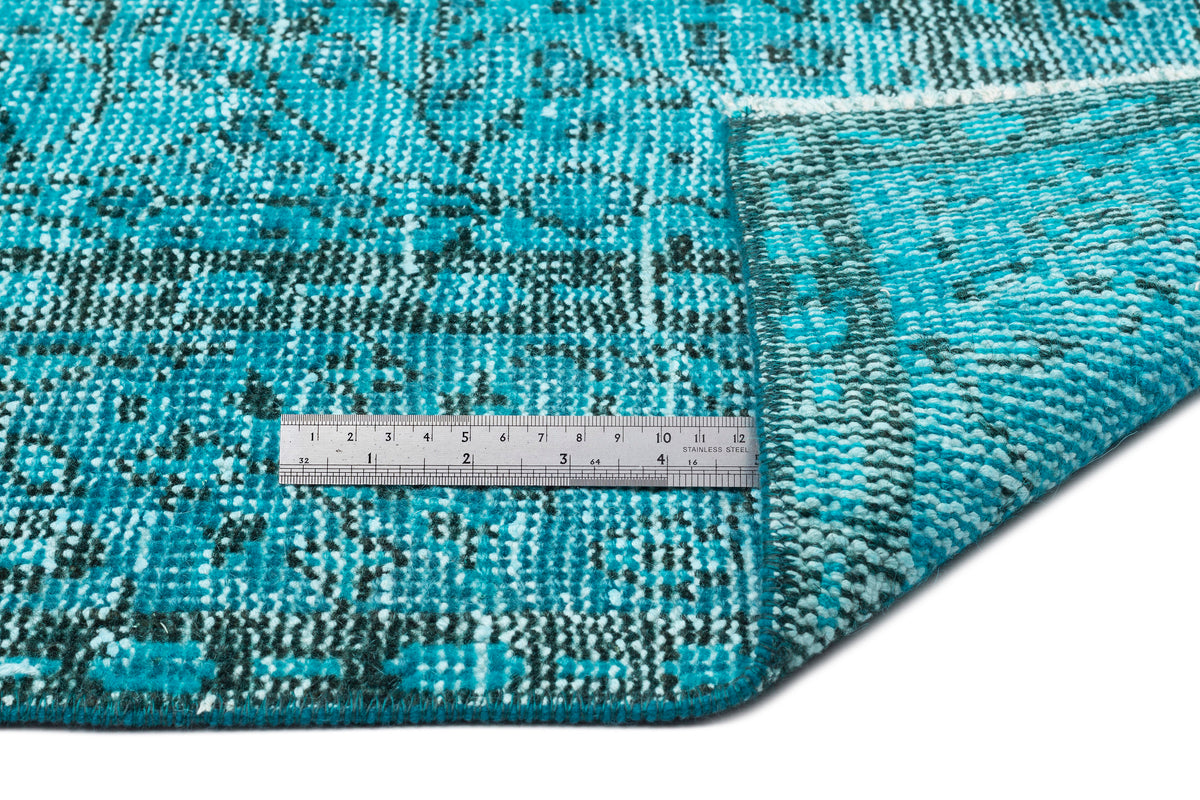 Turquoise and black distressed medallion rug with a folded corner and a metal ruler for scale on a white background.