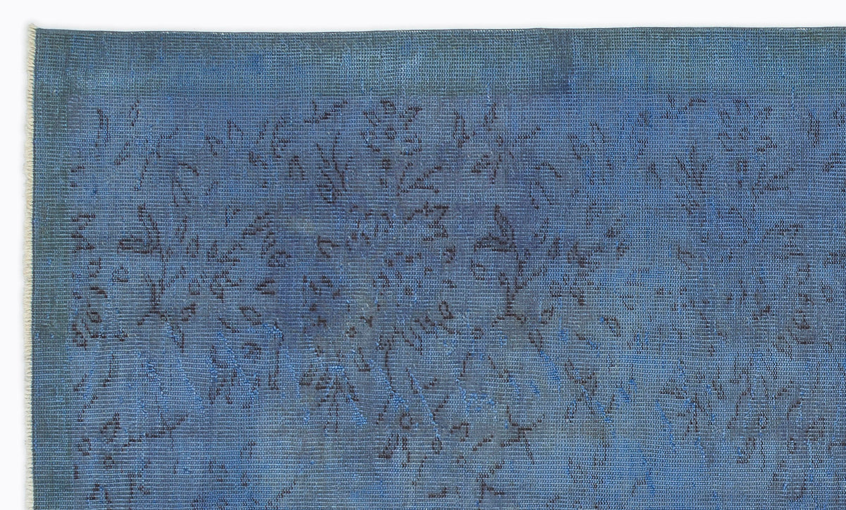 Deep blue vintage-style rug with a faded, dark floral pattern and visible fringe edge.