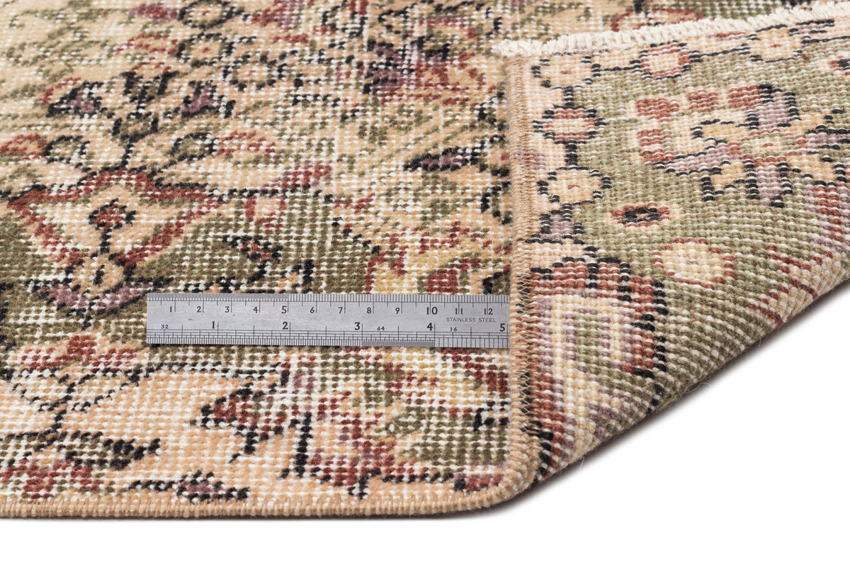 Distressed beige, green, and red floral medallion rug with a metal ruler for scale on a white background.