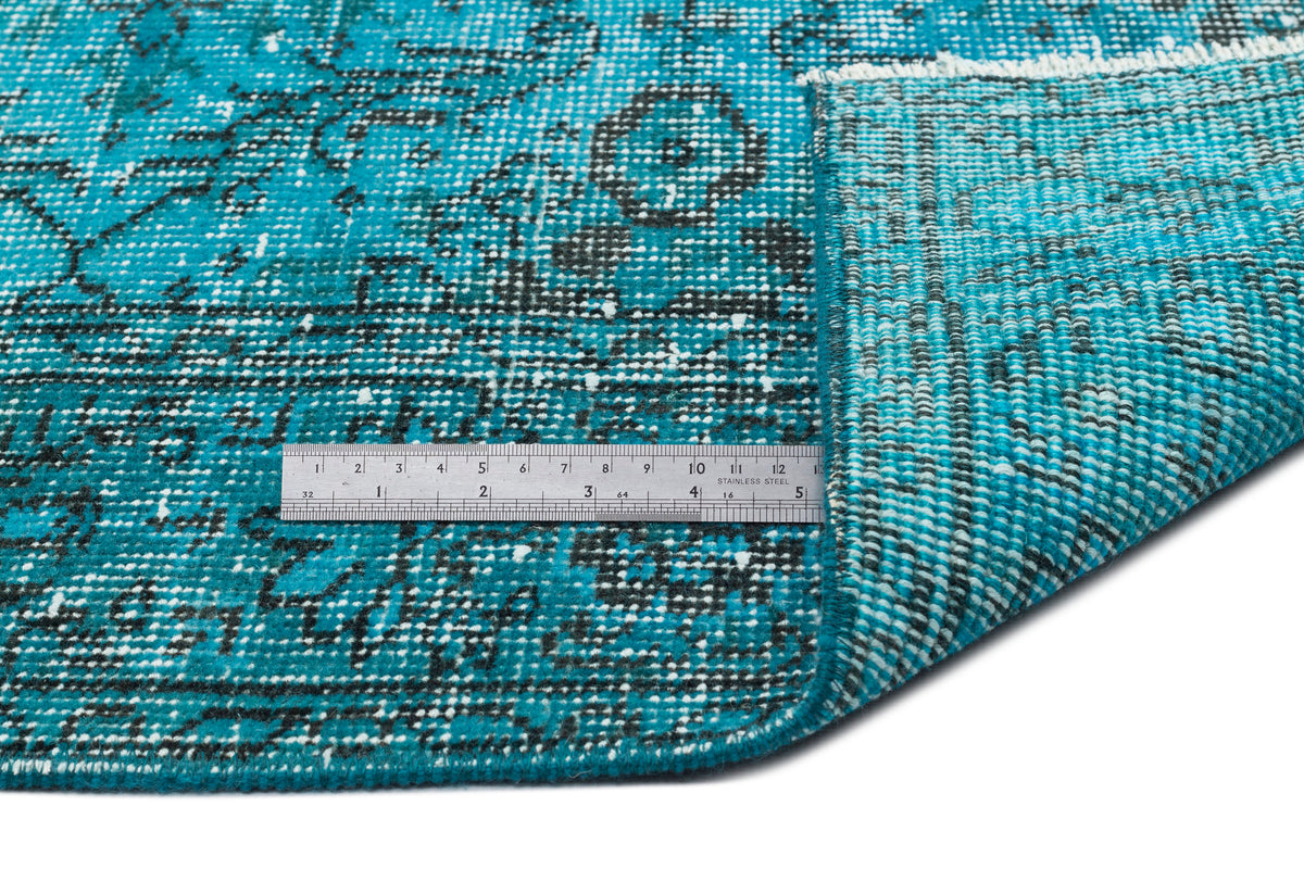 Turquoise and black distressed traditional rug with a folded corner and a metal ruler for scale.