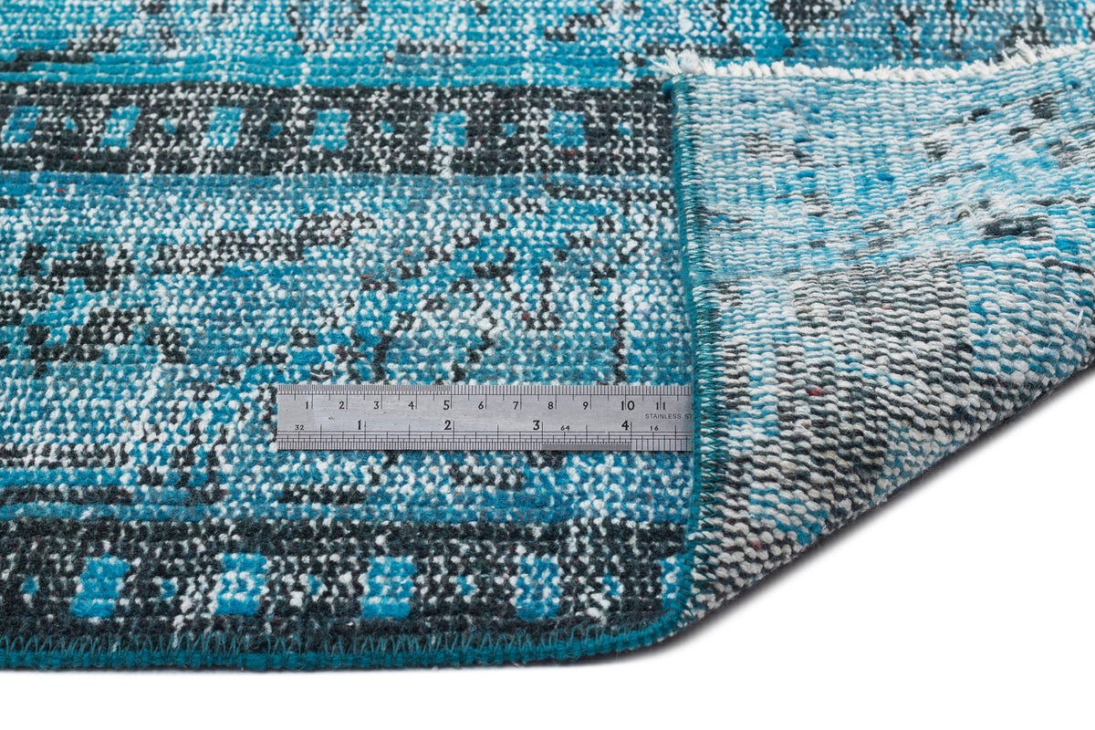 Turquoise, black, and white distressed geometric rug with a folded corner and a metal ruler for scale.