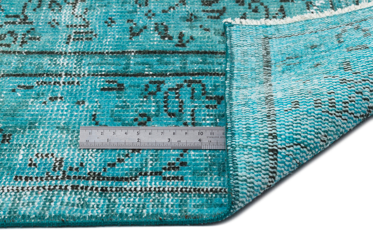 Turquoise and black distressed traditional rug with a folded corner and a metal ruler for scale on a white background.