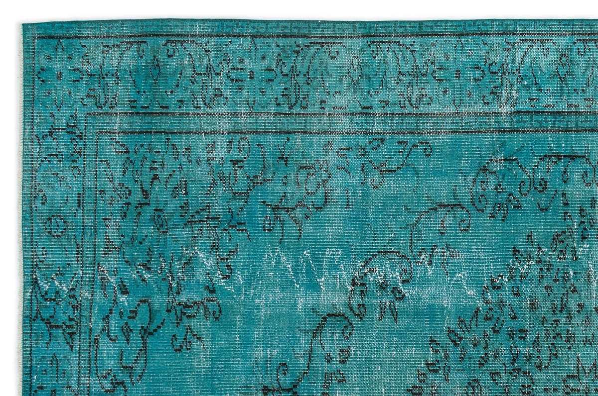 Teal rug with a distressed black floral pattern and a decorative border.