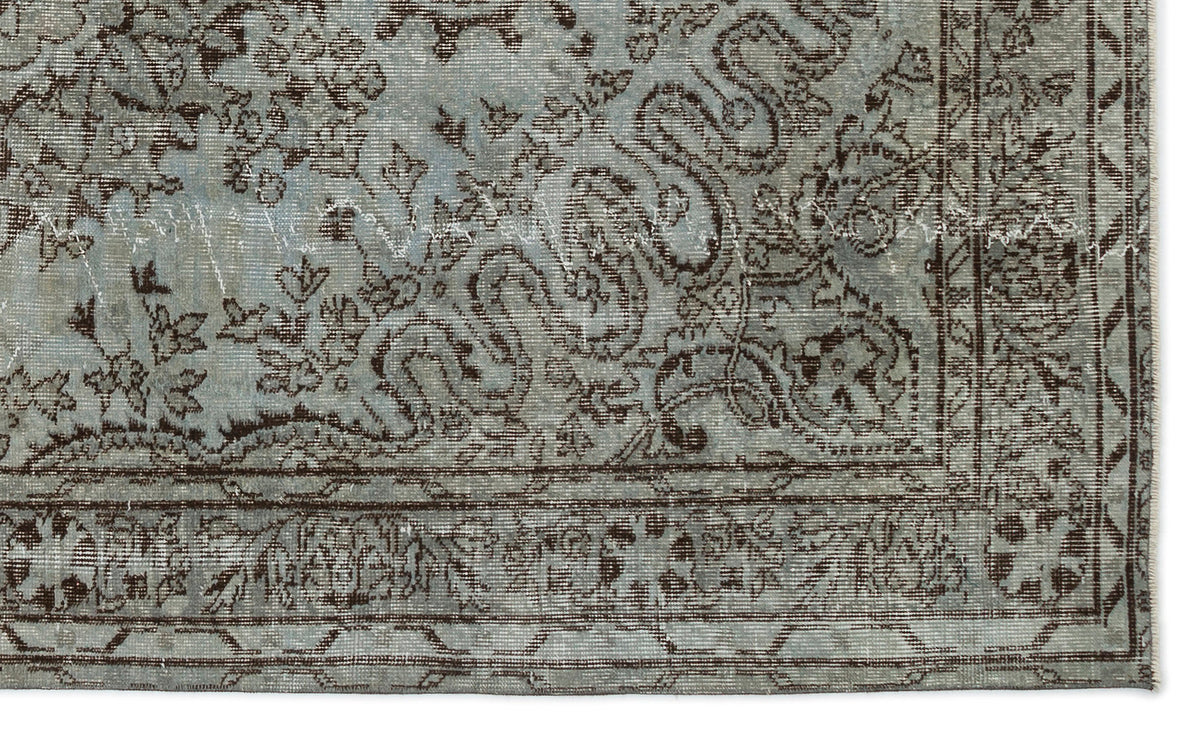 Light blue and dark brown distressed rug with a traditional floral and scrollwork pattern and a geometric border.