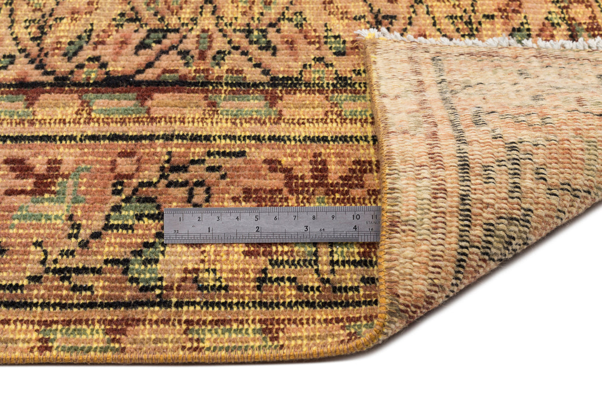 Rust, yellow, and green traditional patterned rug with a folded corner revealing the underside and a metal ruler.