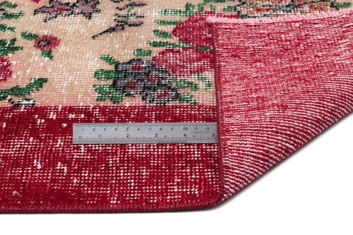 Load image 1 in gallery view. Beige and red floral patterned rug with a distressed texture, shown folded to reveal the underside and a metal ruler.