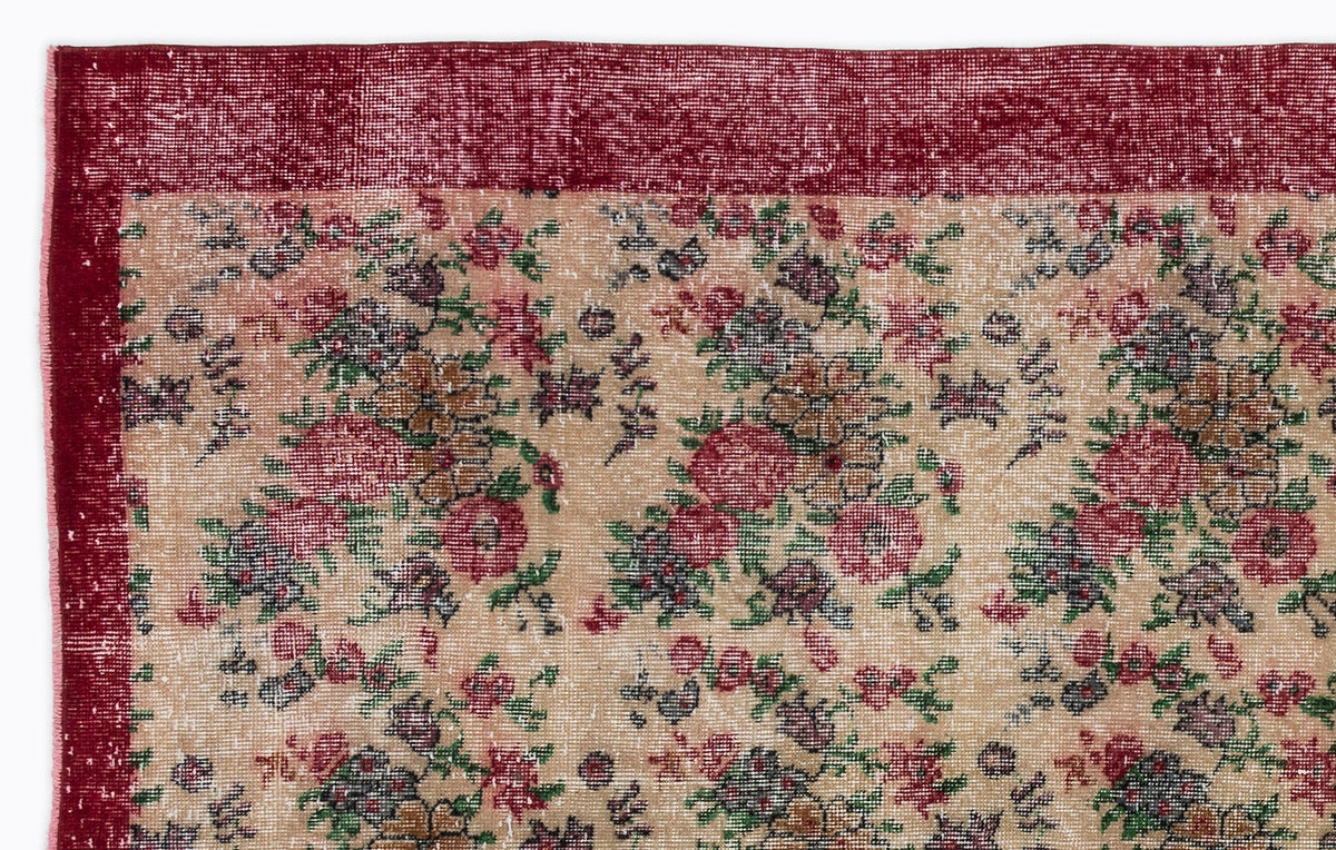 Distressed beige rug with a red border and a repeating floral pattern in shades of red, green, and dark brown.