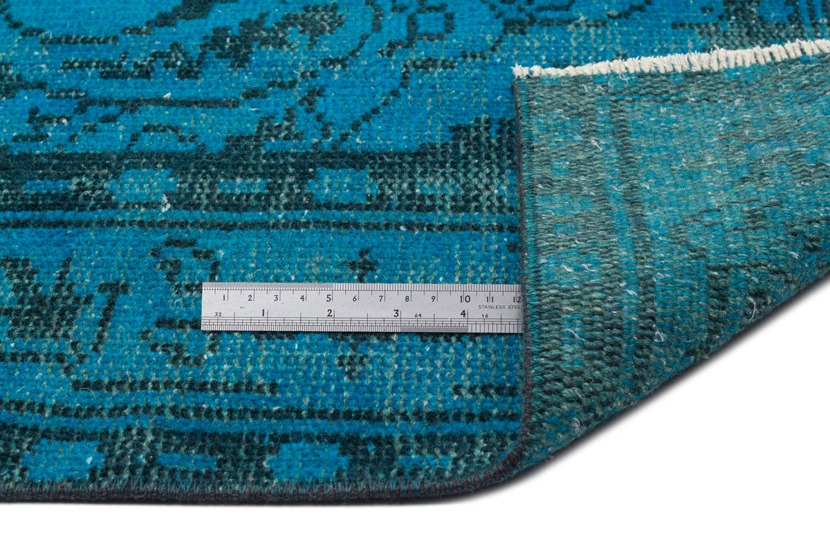 Teal and dark blue distressed traditional rug with a folded corner and a metal ruler for scale.
