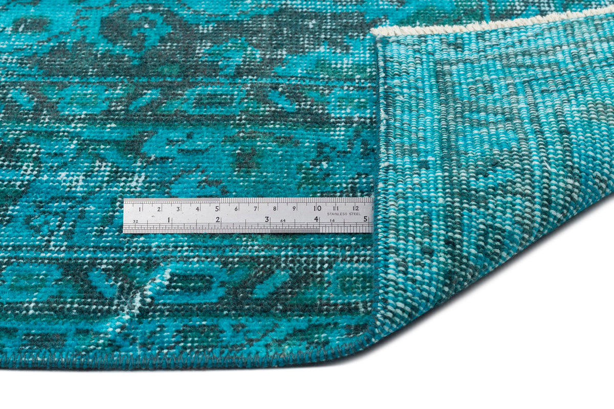 Teal and dark green distressed medallion rug with a folded corner and a stainless steel ruler for scale.