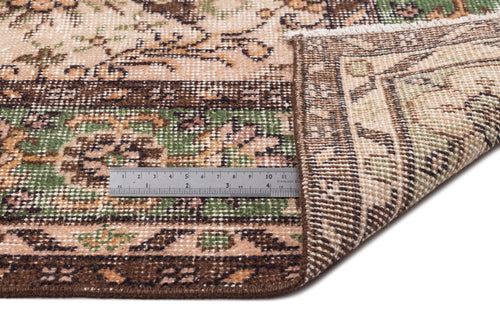 Load image 1 in gallery view. Beige, brown, and green traditional floral patterned rug with a folded corner and a metal ruler for scale.
