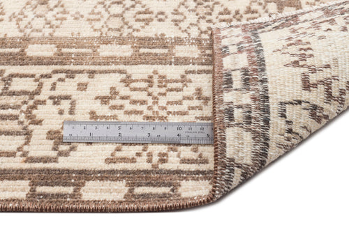 Load image 1 in gallery view. A close-up of the Kidaen - Vintage Medallion Rug (6'0 x 9'6) in beige and brown shows one corner folded to reveal the backing, with a metal ruler on top measuring about 6 inches.