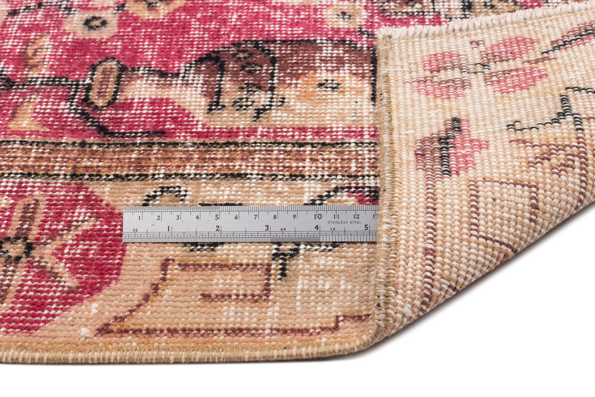 Magenta and beige vintage-style rug with a geometric pattern, showing the pile and woven backing with a metal ruler.