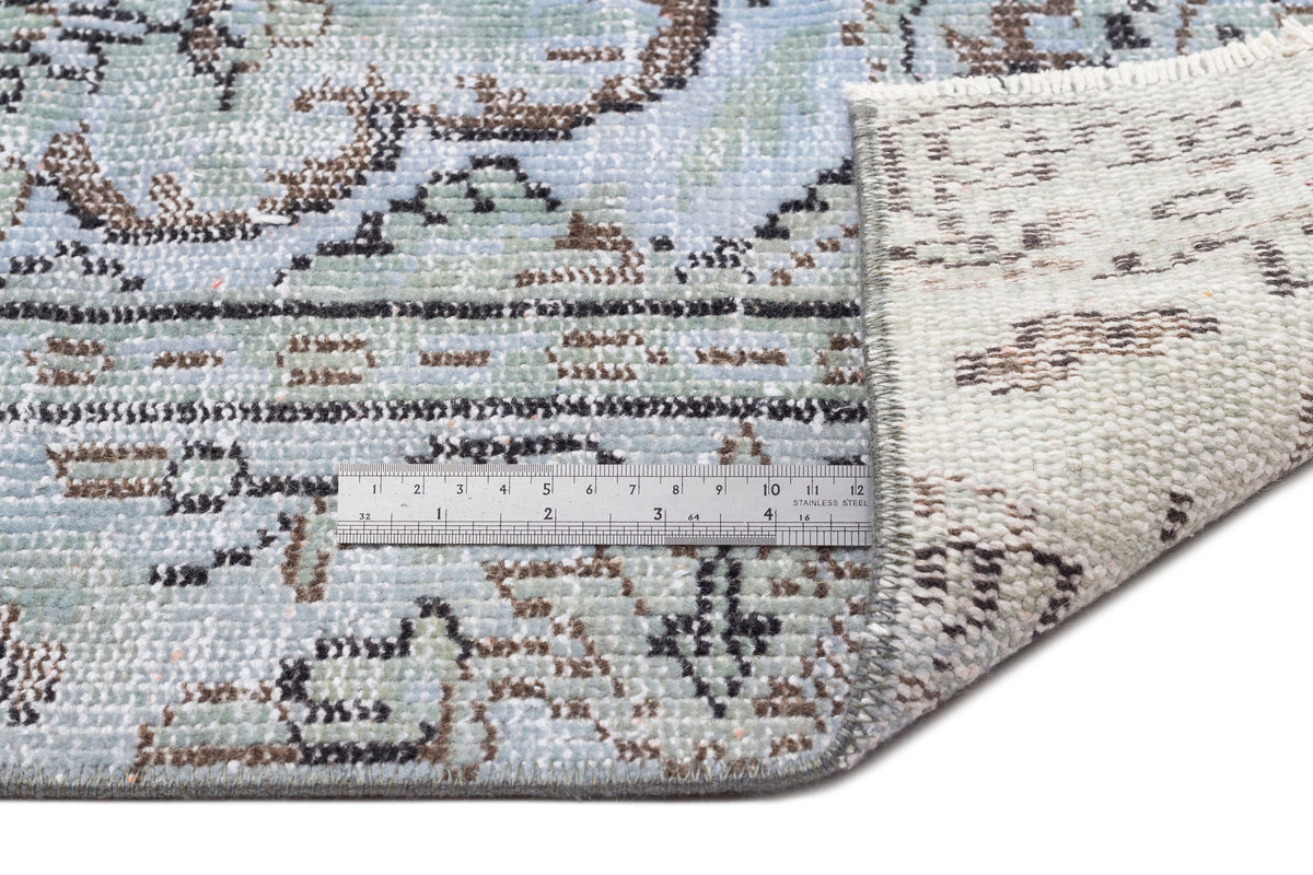 Light blue and cream distressed rug with a traditional floral pattern and a metal ruler showing pile texture.