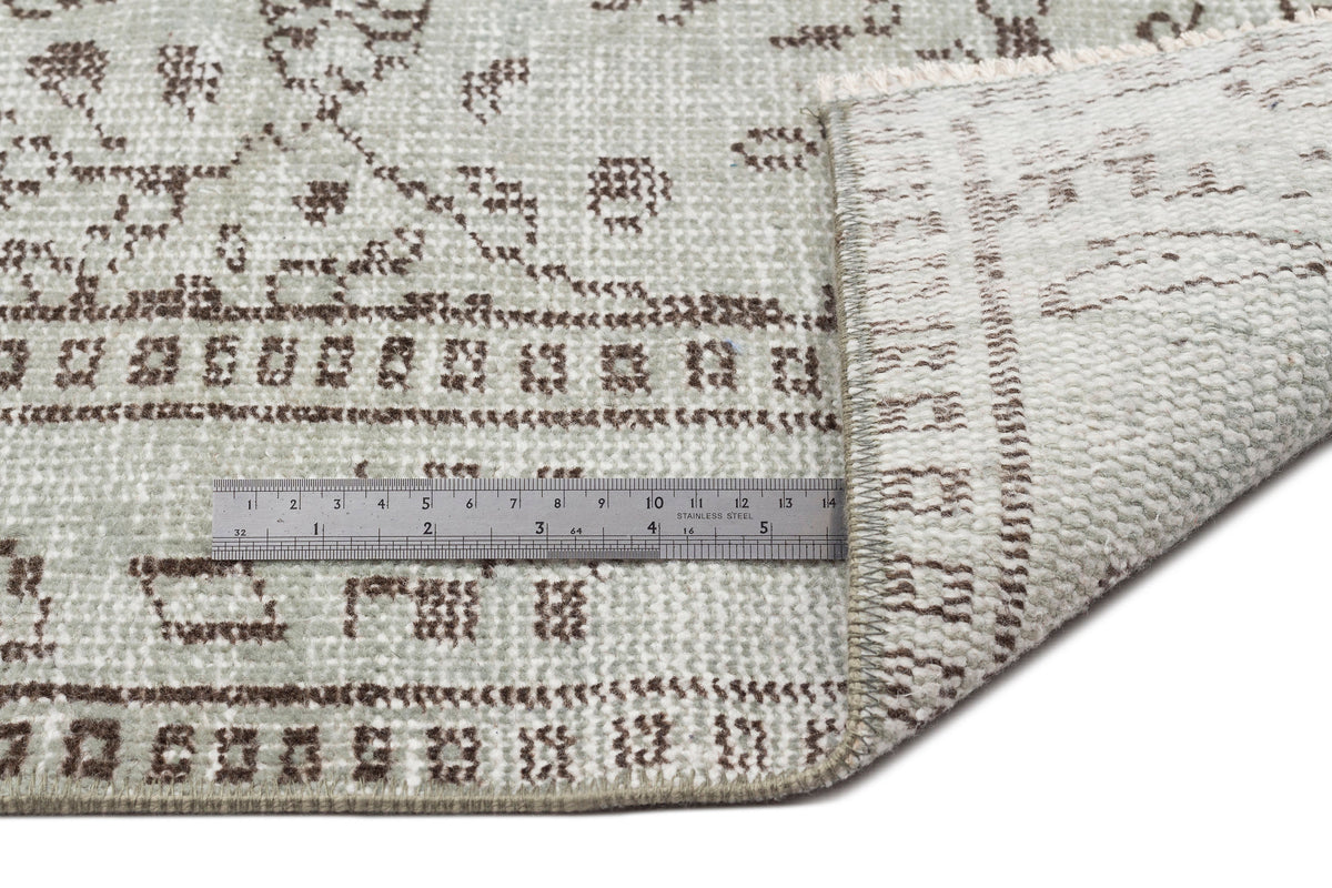Sage green and brown distressed rug with a traditional pattern, shown with a metal ruler for scale.