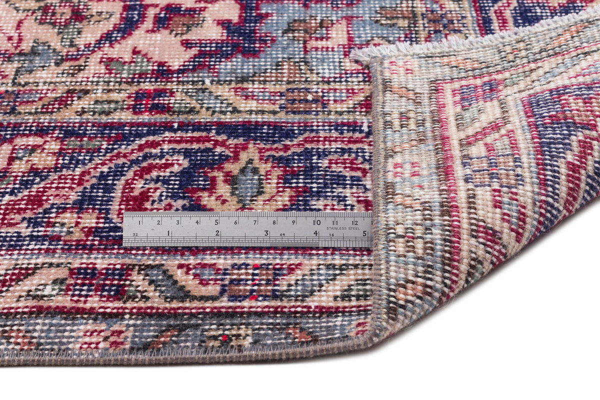 Traditional Persian-style rug with a floral medallion pattern in navy, red, and beige, shown with a metal ruler.
