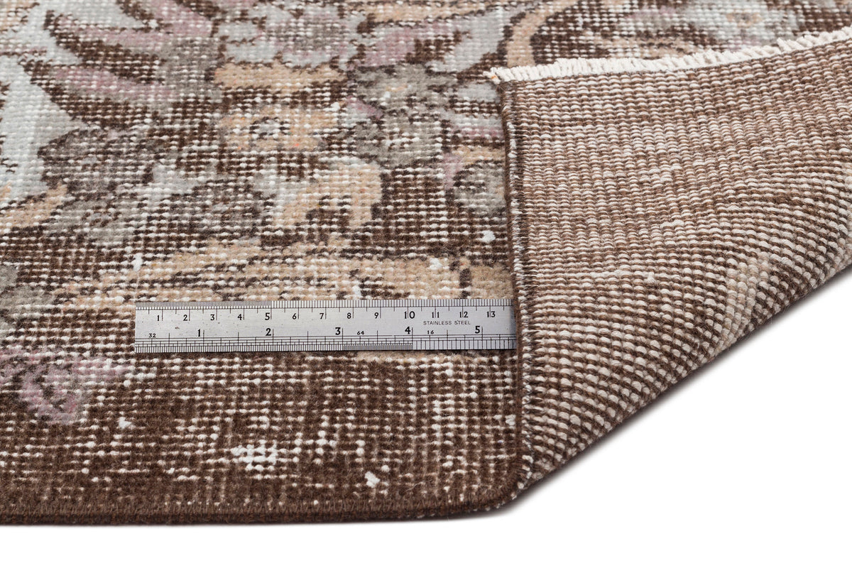 Brown and beige distressed floral rug with a folded corner and a stainless steel ruler for scale.