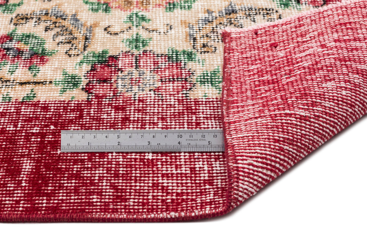 Cream and red floral patterned rug with a folded corner and a stainless steel ruler for scale.
