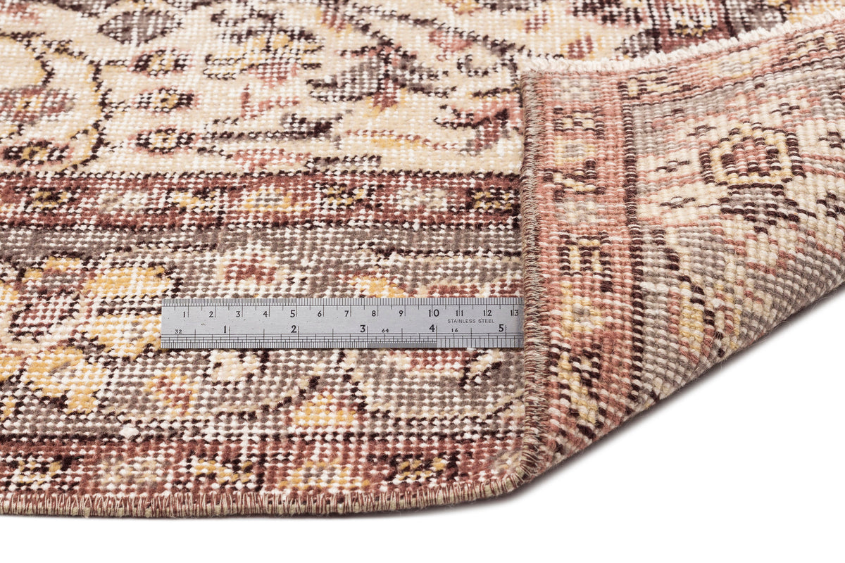 Distressed beige, brown, and muted red traditional rug with a folded corner and a metal ruler for scale.