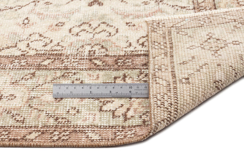 Load image 1 in gallery view. A close-up of the Glela - Vintage Floral Rug (5'0 x 8'11) in beige and brown, with a corner folded to show the underside. A metal ruler beside the fold highlights its thickness and intricate vintage floral design.