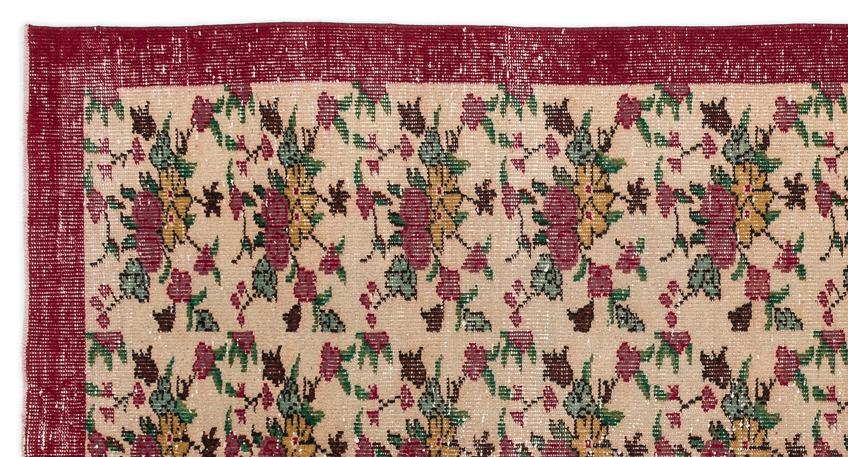 Beige rug with a red border and a repeating floral pattern in red, yellow, and green on a white background.