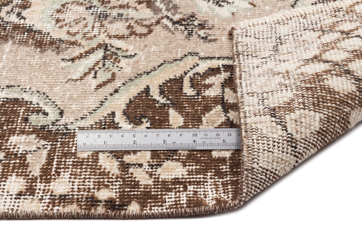 Beige and brown traditional floral medallion rug with a folded corner and a stainless steel ruler for scale.