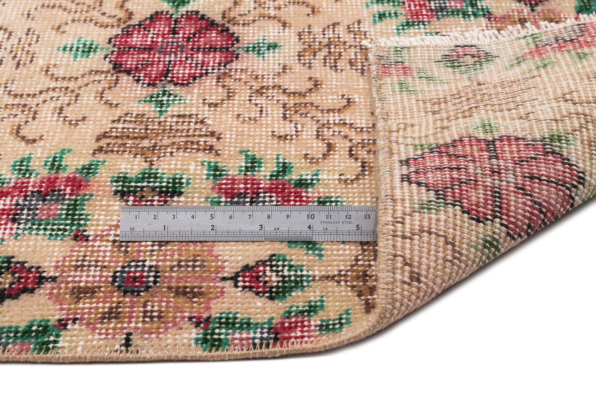Beige rug with a red and green floral pattern, shown with a metal ruler for scale and a folded corner.