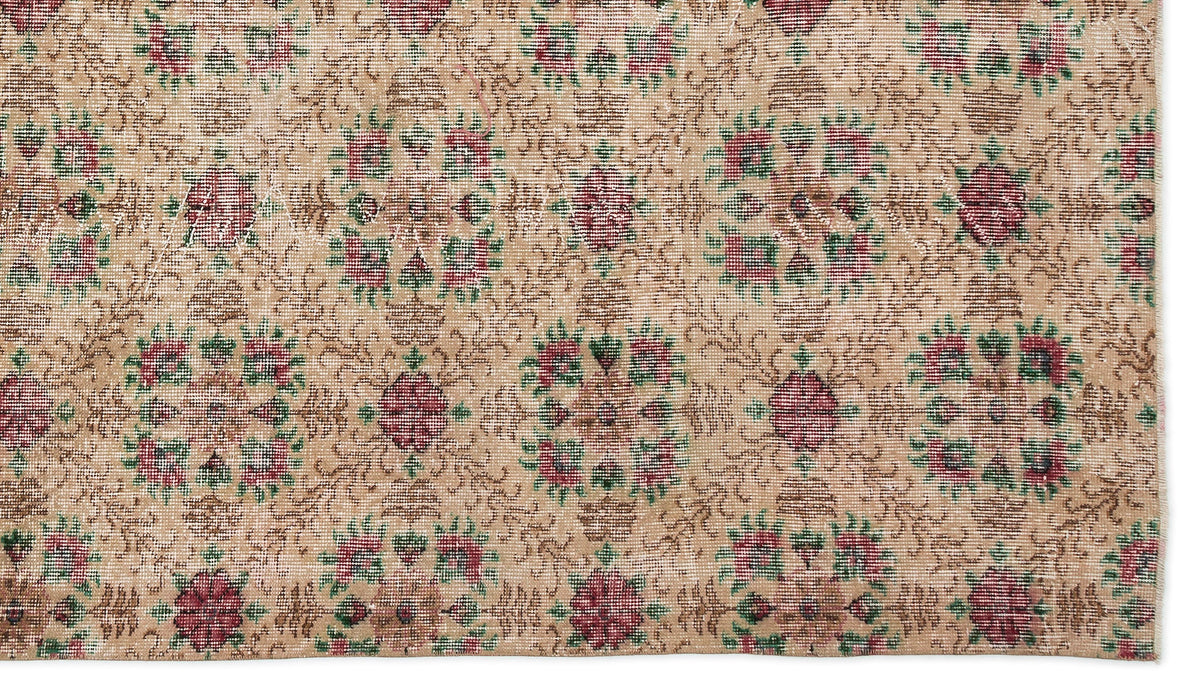 Tan vintage rug with a repeating floral medallion pattern in muted red and green, featuring a distressed texture.