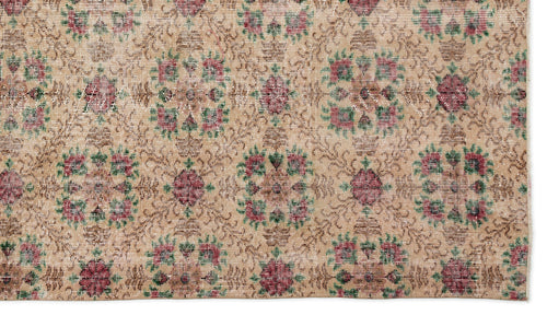 Load image 1 in gallery view. Tan vintage rug with a repeating floral medallion pattern in muted red and green, featuring a distressed texture.