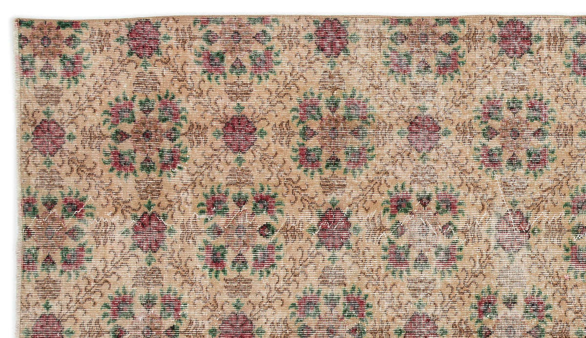 Tan vintage-style rug with a repeating floral medallion pattern in muted red and green on a distressed background.