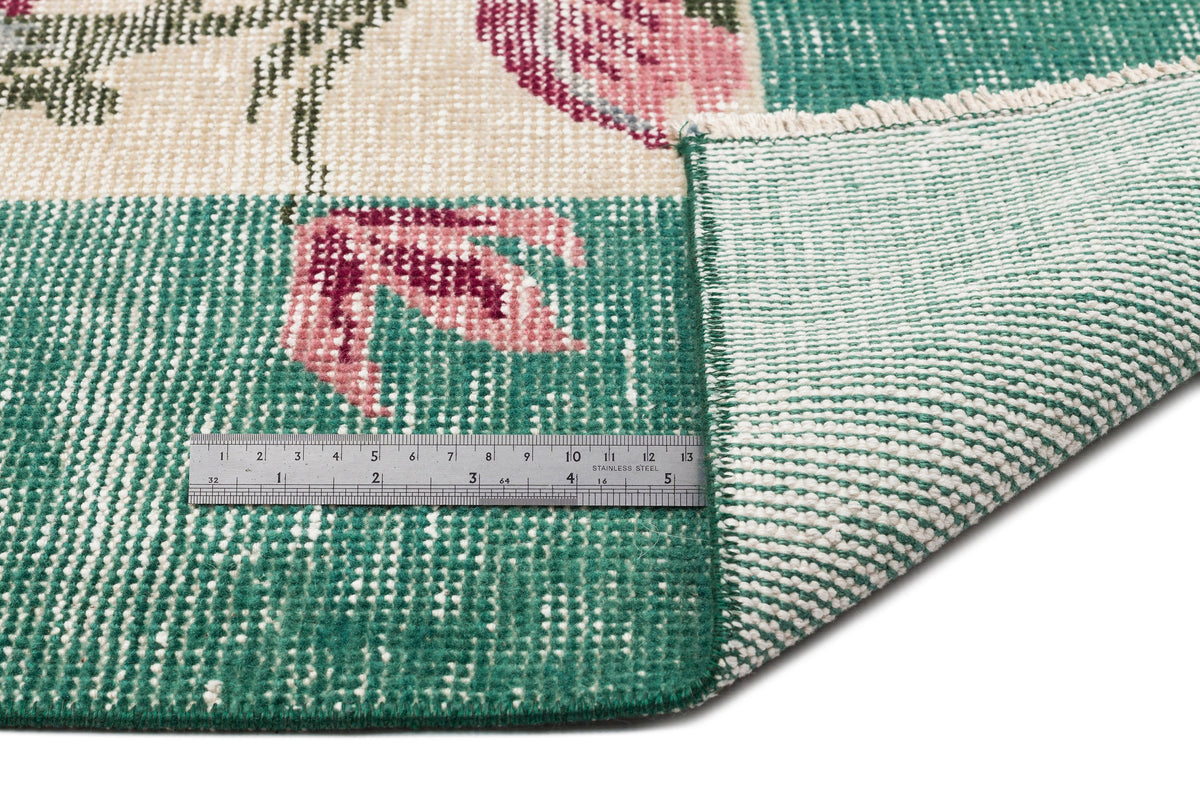 Green and cream floral rug with a folded corner and a stainless steel ruler for scale.