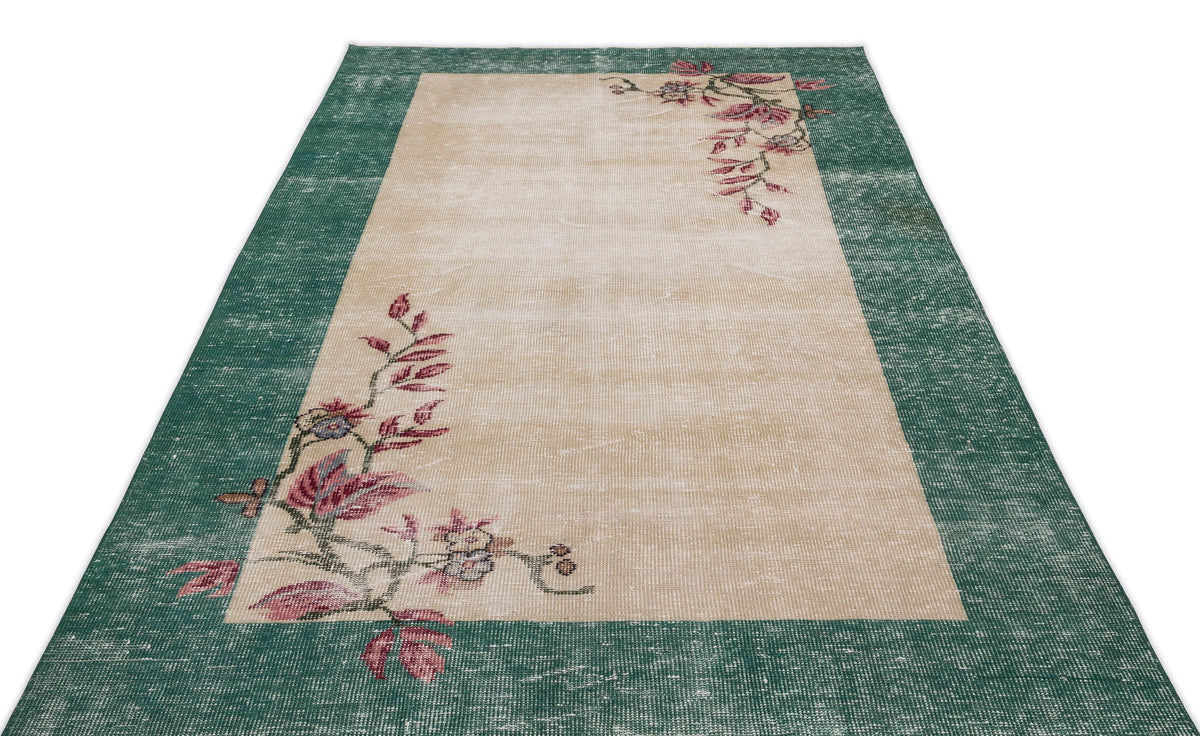 Distressed beige rug with a wide green border and asymmetrical floral vine pattern in pink and muted tones.