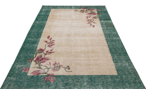 Load image 1 in gallery view. Distressed beige rug with a wide green border and asymmetrical floral vine pattern in pink and muted tones.
