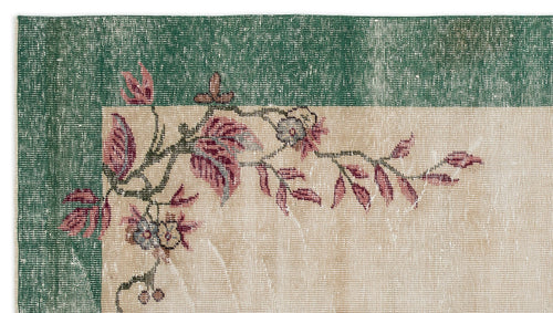 Load image 1 in gallery view. Distressed beige rug with a dark green border and a floral vine pattern in shades of pink and grey.