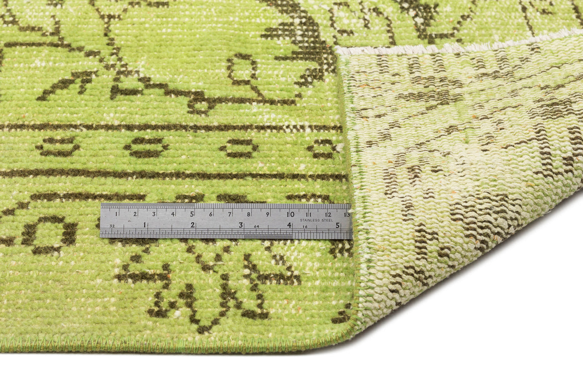 Lime green and dark brown distressed traditional rug with a folded corner and a metal ruler for scale.