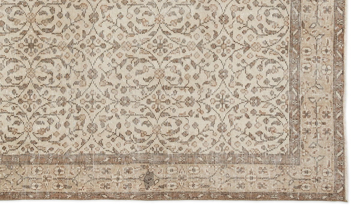 The Pavia - Vintage Floral Rug (5'7 x 9'5) is a beige and brown overdyed Anatolian hand-woven rug with geometric and floral designs, a wide patterned border, and a subtly distressed texture for vintage character.