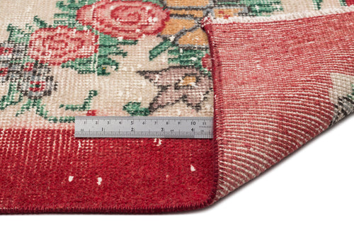 Load image 1 in gallery view. Distressed floral rug in red, green, and beige with a folded corner revealing the red backing and a metal ruler for scale.