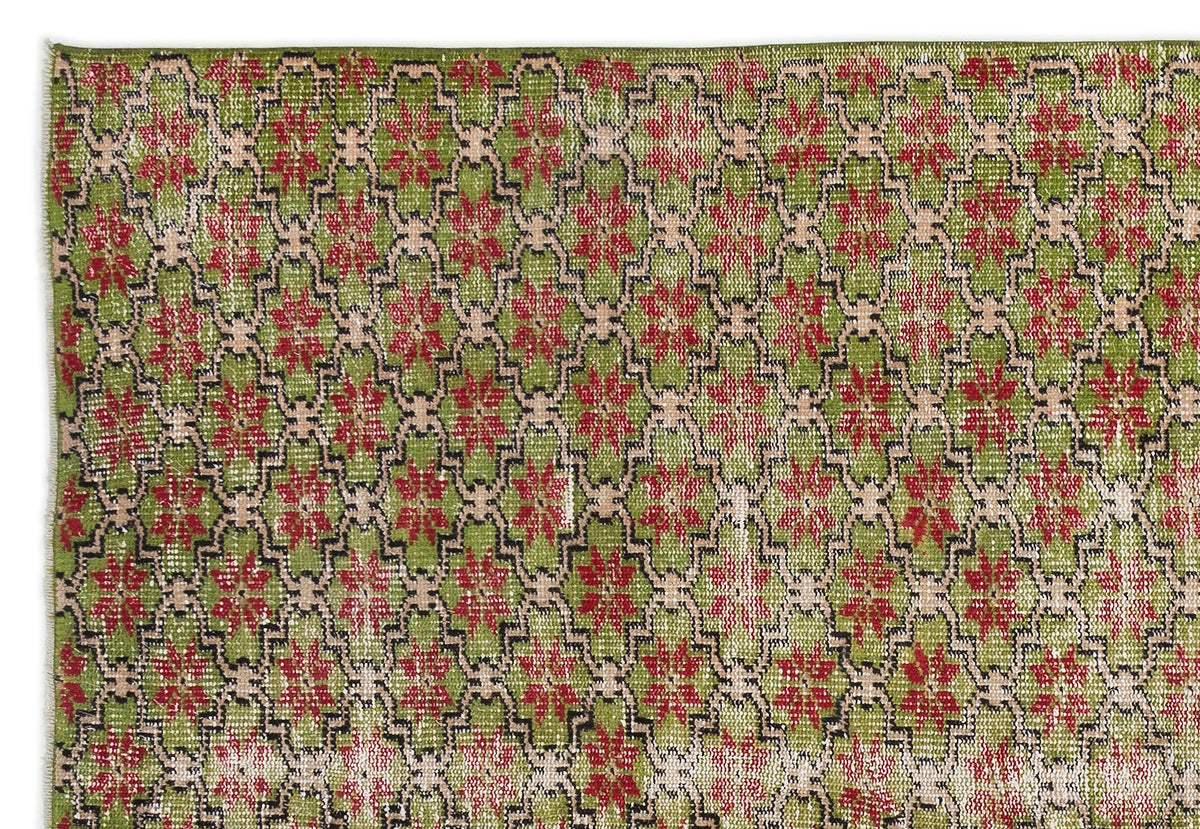 Green rug with a repeating red floral medallion pattern outlined in black and beige geometric lattice.