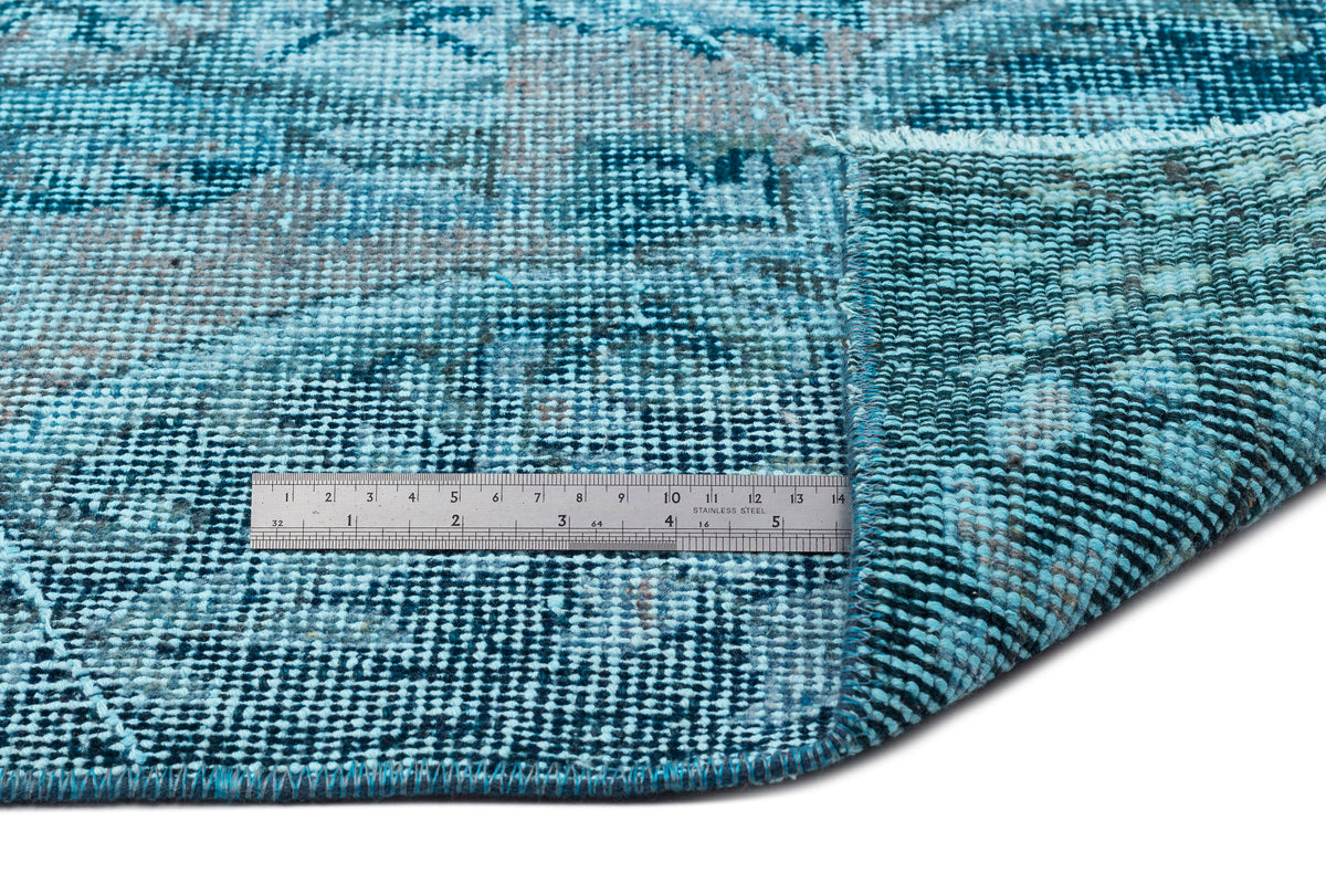 Distressed teal and blue patterned rug with a folded corner and a stainless steel ruler for scale.