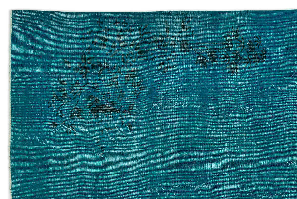 Teal distressed rug with a faded black floral motif and visible woven texture on a white background.