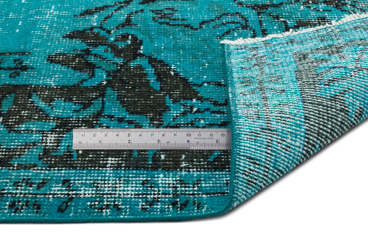 Teal and black distressed floral pattern rug with a folded corner and a metal ruler for scale.
