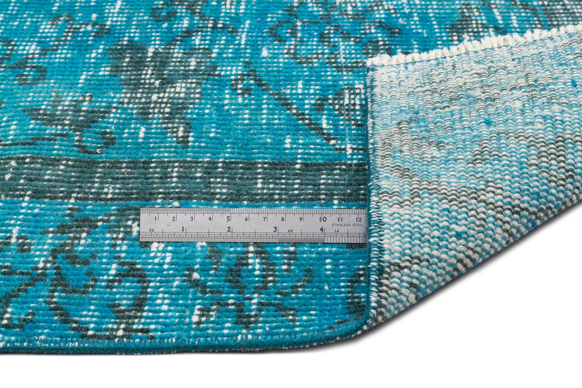 Teal and dark grey distressed medallion rug with a white fringe, shown with a metal ruler for scale.