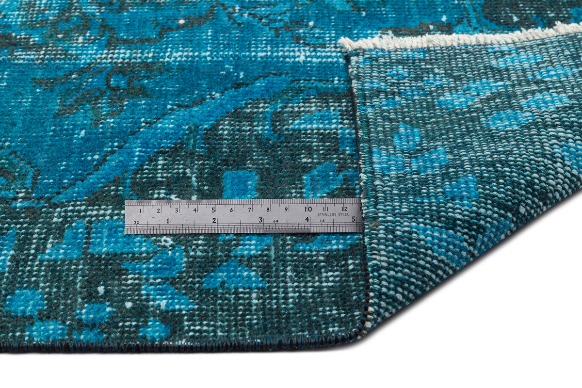 Distressed teal and navy blue rug with a traditional medallion pattern, shown folded with a metal ruler for scale.