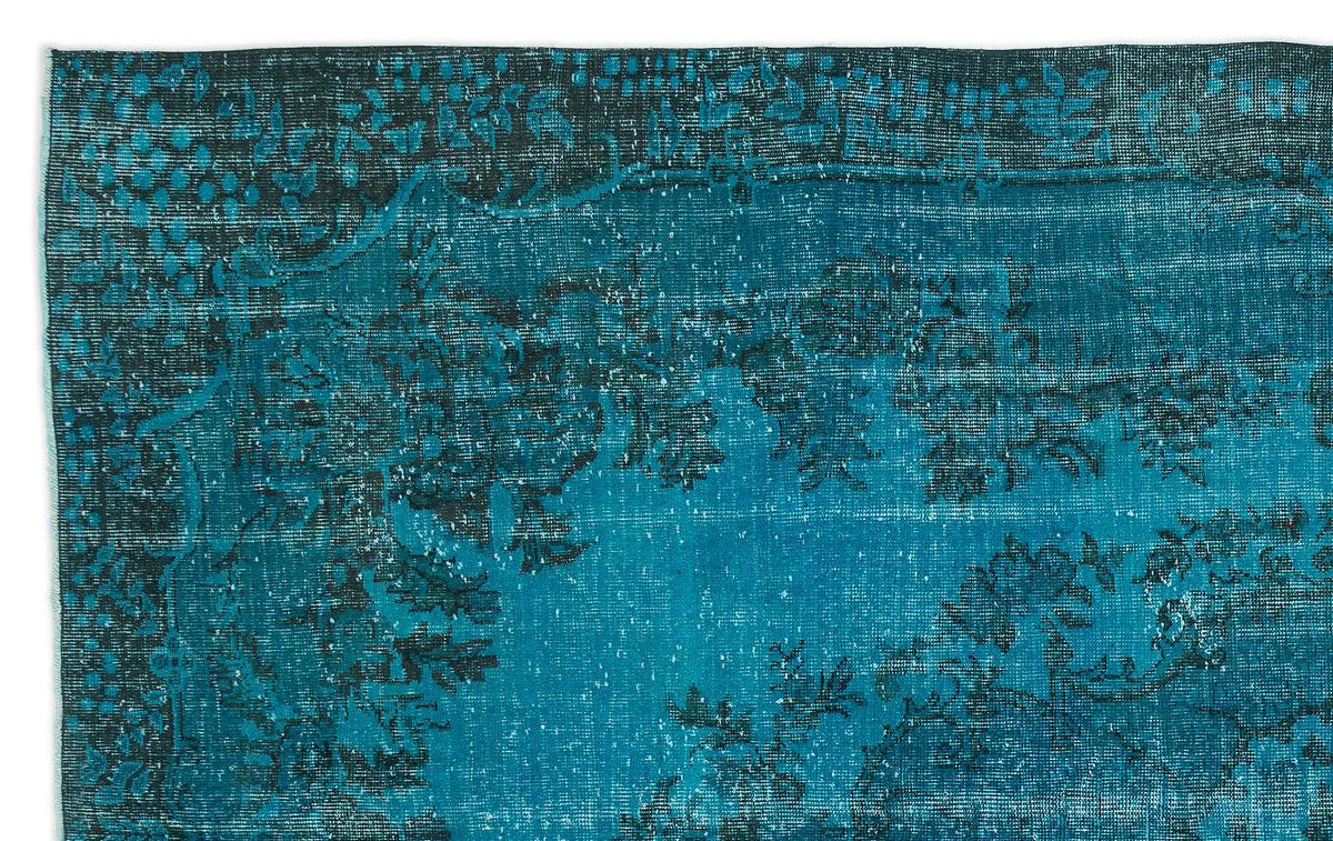 Teal and black distressed rug with a traditional floral border and faded central medallion pattern.